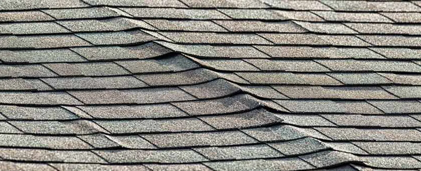 Close-up of damaged asphalt roof shingles showing buckling and warping from possible water or heat damage.