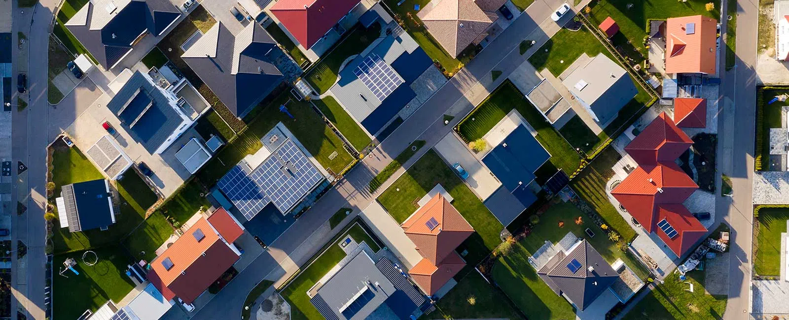 Aerial view of a suburban neighborhood with houses featuring solar panels and red roofs on a sunny day