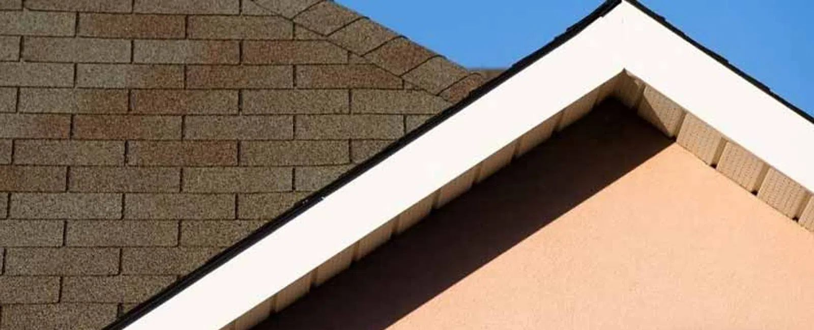 Close-up of brown shingle roof and beige wall under clear blue sky with Balken Roofing logo.
