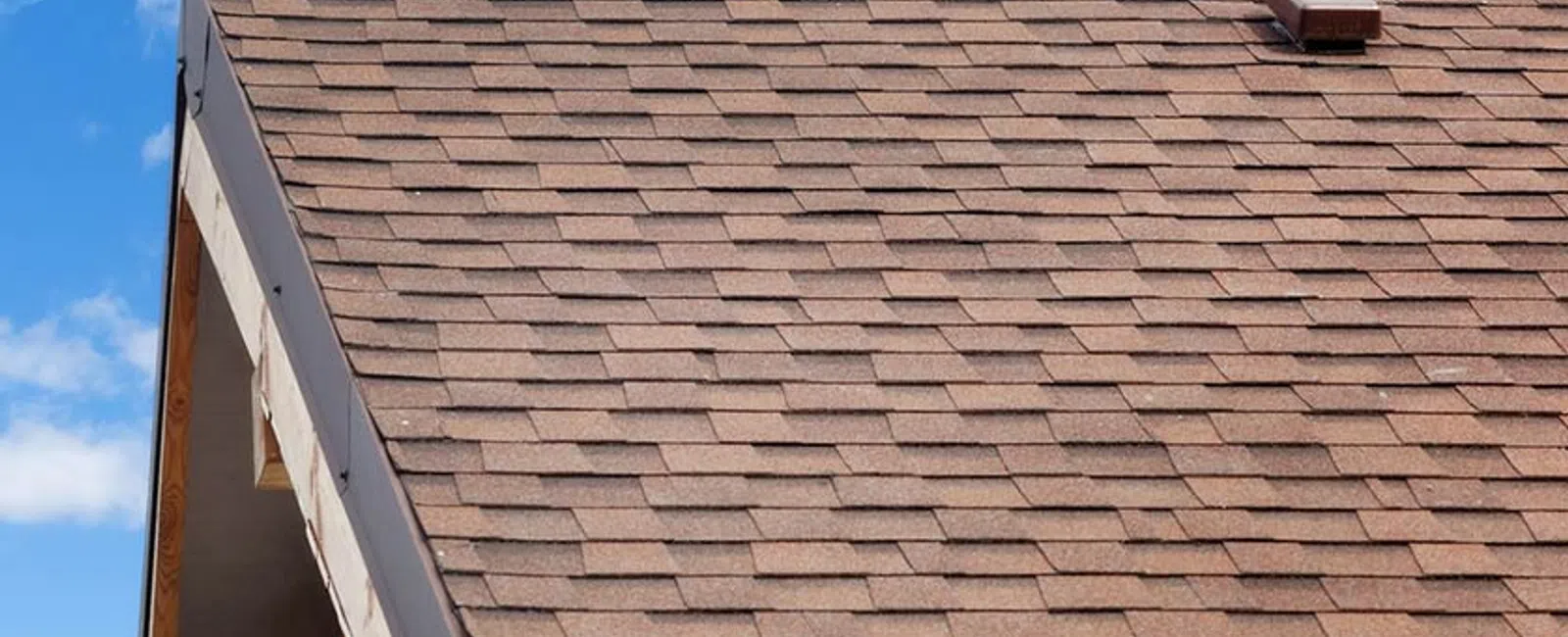 Close-up of a brown shingle roof under a blue sky with scattered clouds.