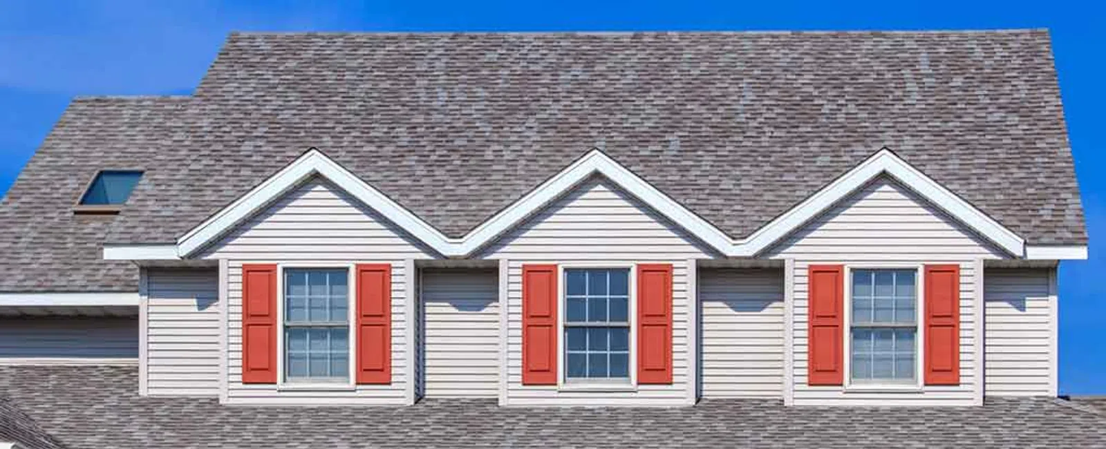 Modern house with gray shingle roofing, beige siding, red window shutters, and clear blue sky background.