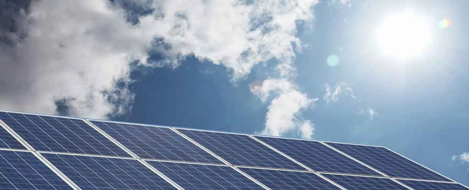 Solar panels angled under a bright sun with blue sky and scattered clouds, promoting renewable energy.