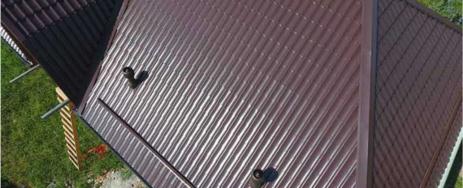 Aerial view of a shiny brown metal roof with vents surrounded by greenery and Balken Roofing logo.