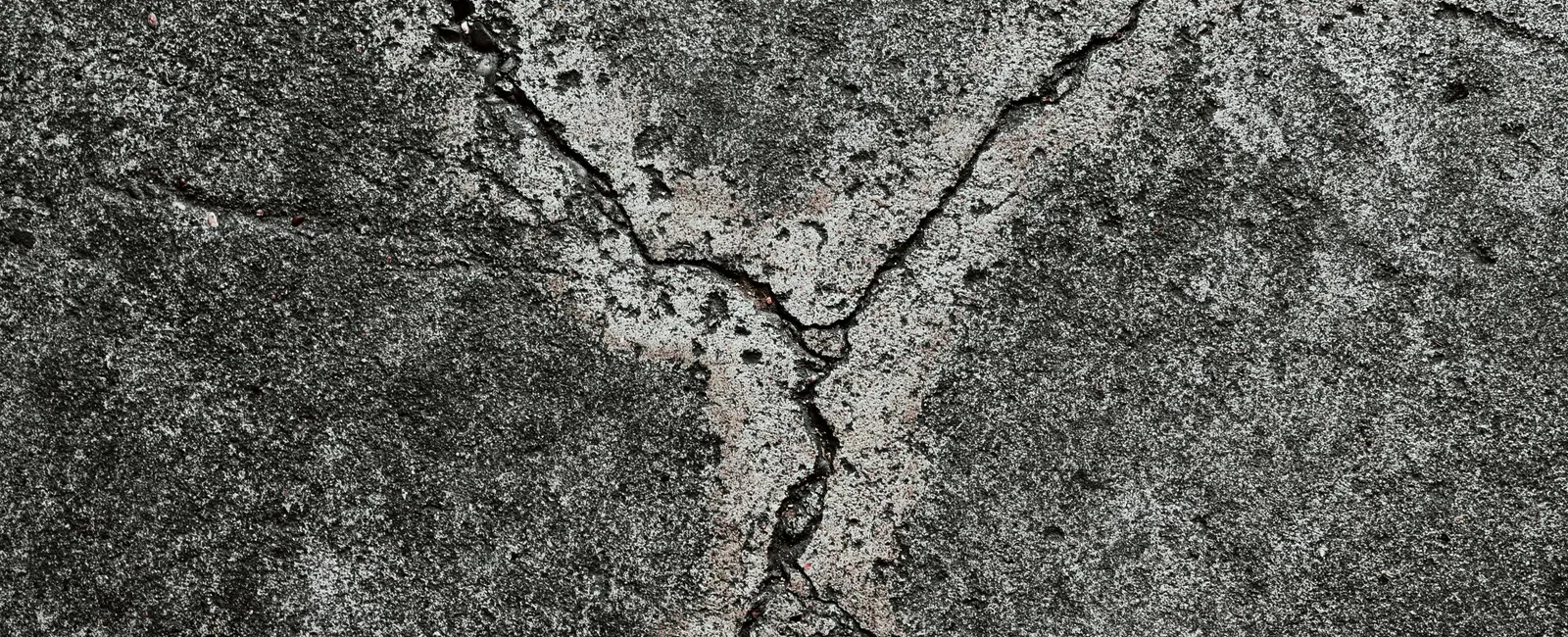 Close-up of cracked, weathered gray concrete surface with rough texture and small debris.