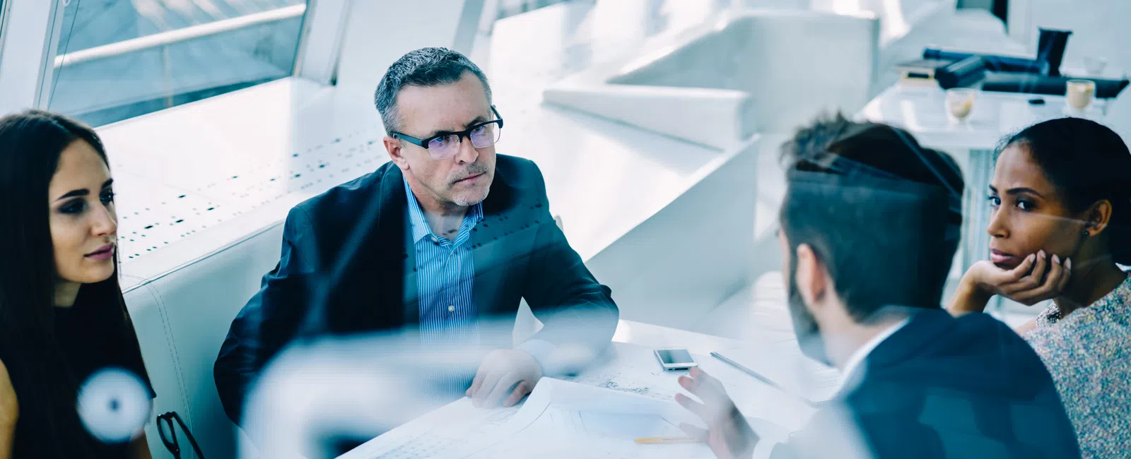 Four professionals discussing blueprints and documents around a bright office table during a meeting.