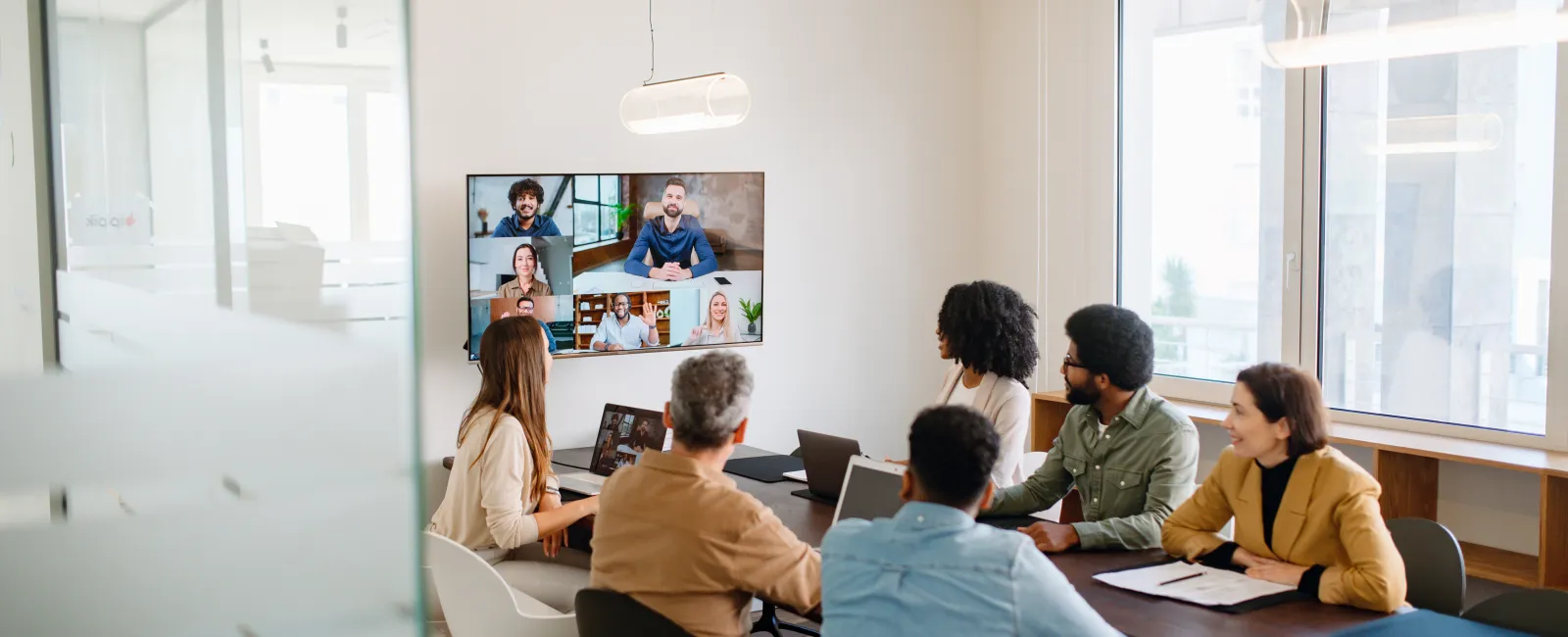 Team in diverse office video conferencing with remote colleagues on large screen meeting room
