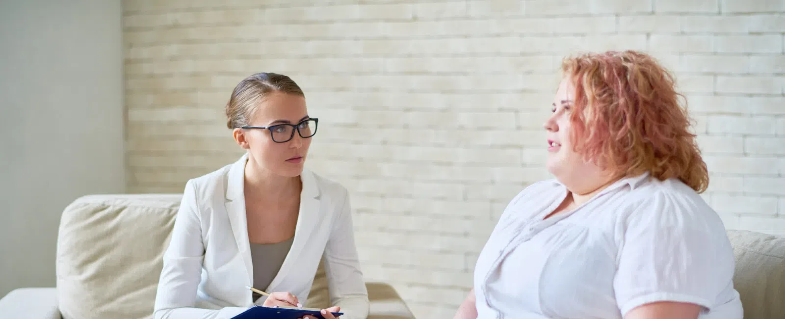 Professional therapist attentively listening to an overweight woman during a counseling session in a bright office.