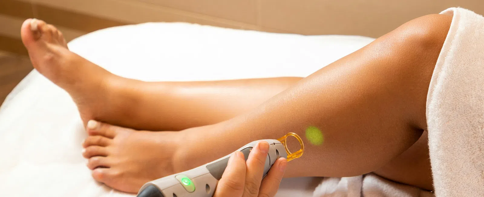 Laser hair removal treatment being performed on a woman's leg in a spa or clinic setting.