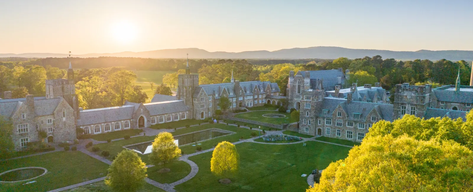 Aerial view of a historic mansion set within lush green grounds at sunset, highlighting architectural elegance.