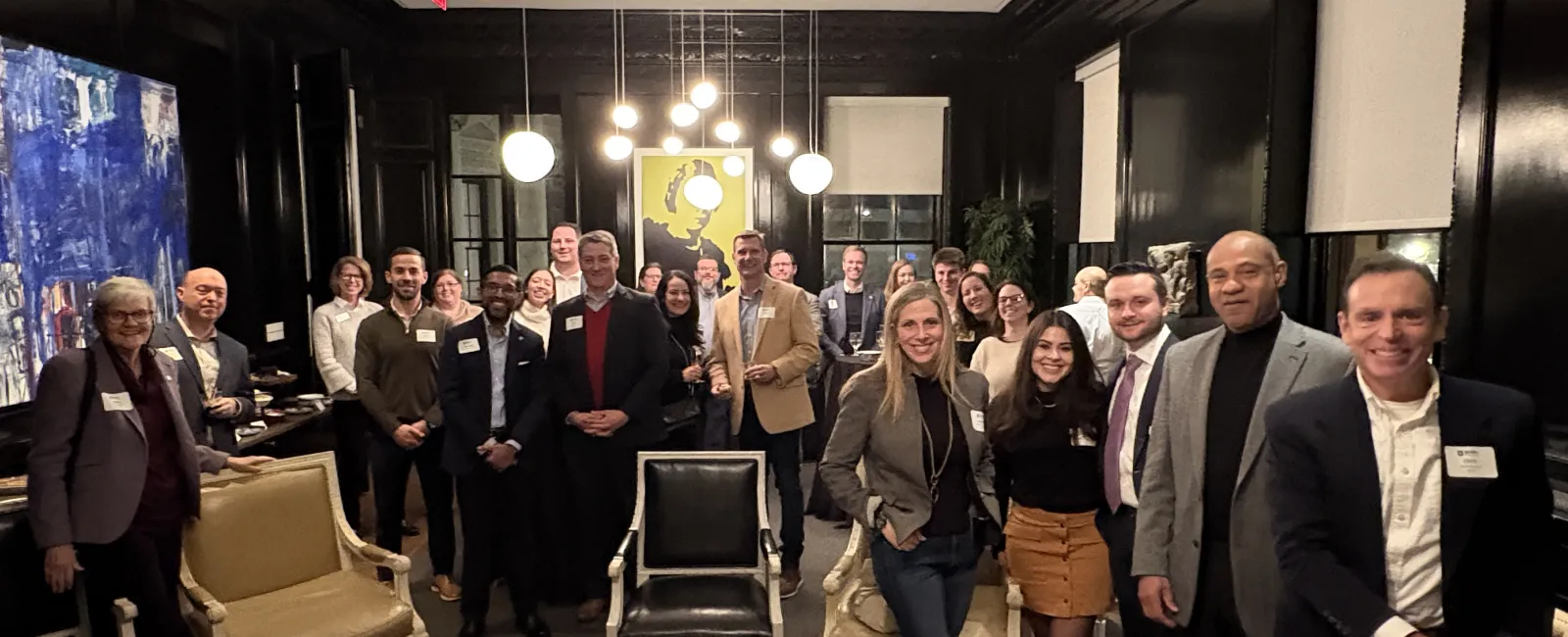 Group of professionally dressed people smiling in a modern, warmly lit room with art and chairs.