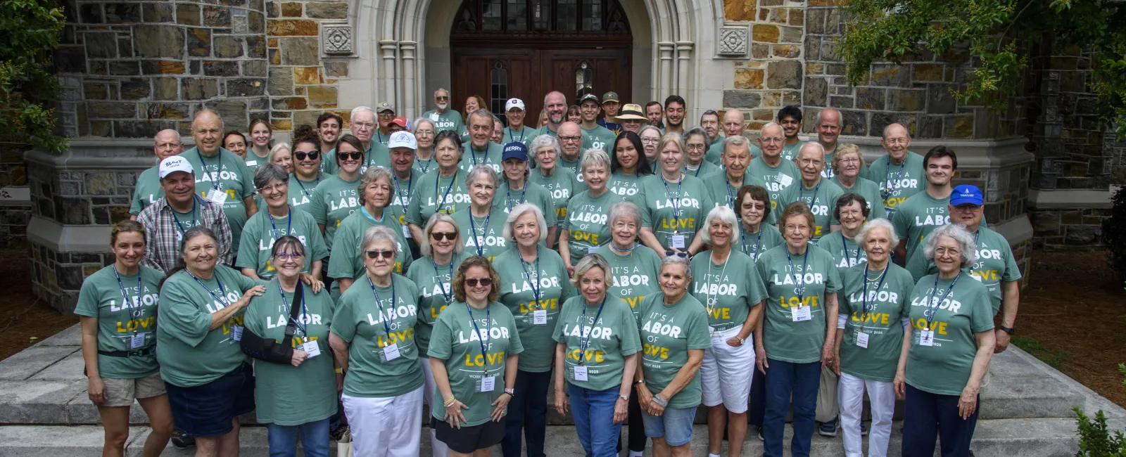 Large group of people wearing matching green Labor of Love shirts standing outside a stone building entrance.