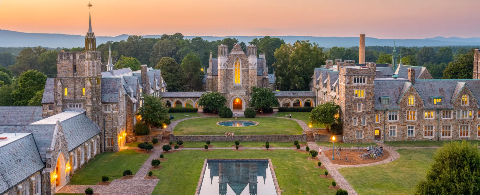Sunset view of a historic college campus with a beautiful reflecting pond and stone buildings.