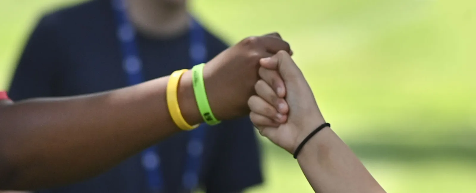 Two people fist bumping outdoors, one with wristbands and the other with a black hair tie on wrist
