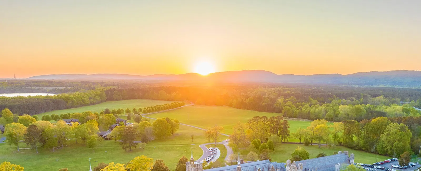 Aerial view of a historic campus at sunset, surrounded by lush greenery and rolling hills.