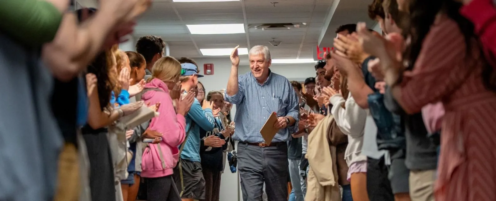 John Grout walking down hallway high-fiving and cheered by people lined up on both sides indoors.