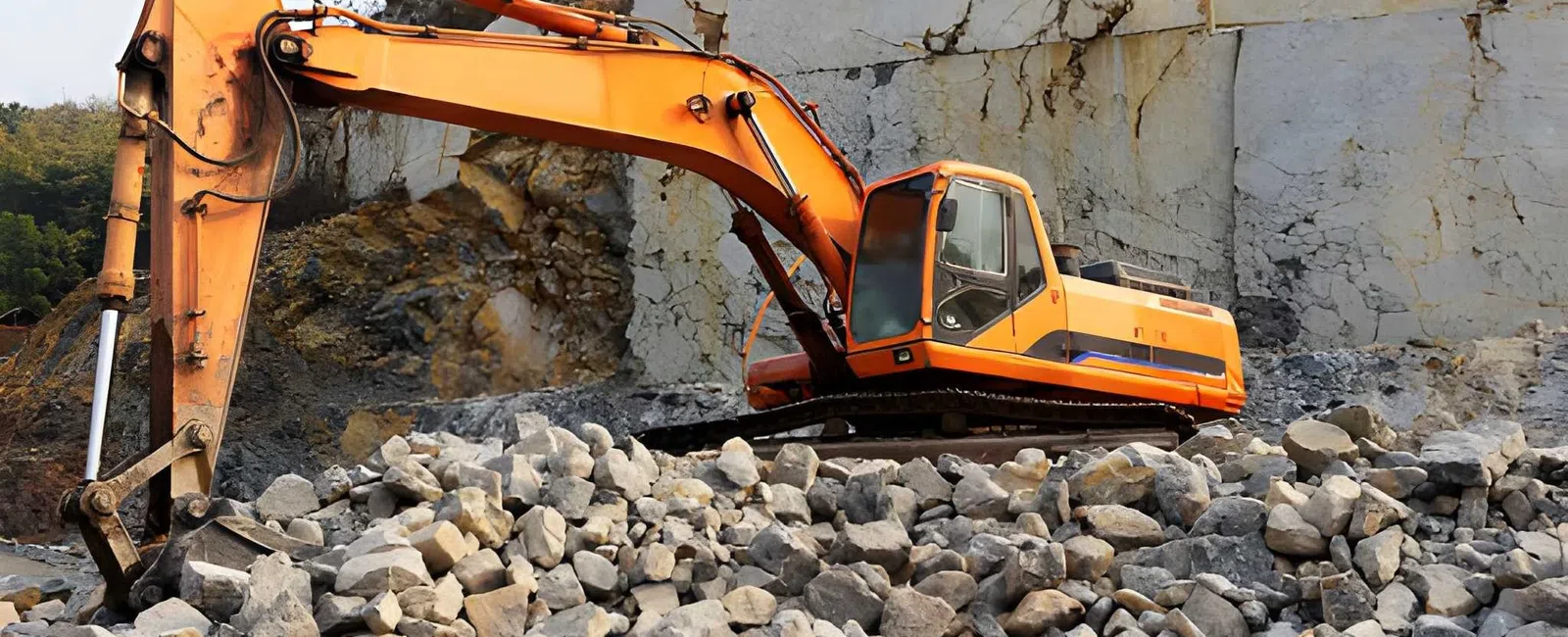 Orange excavator working on a rocky construction site with large stones and cliff background under daylight.