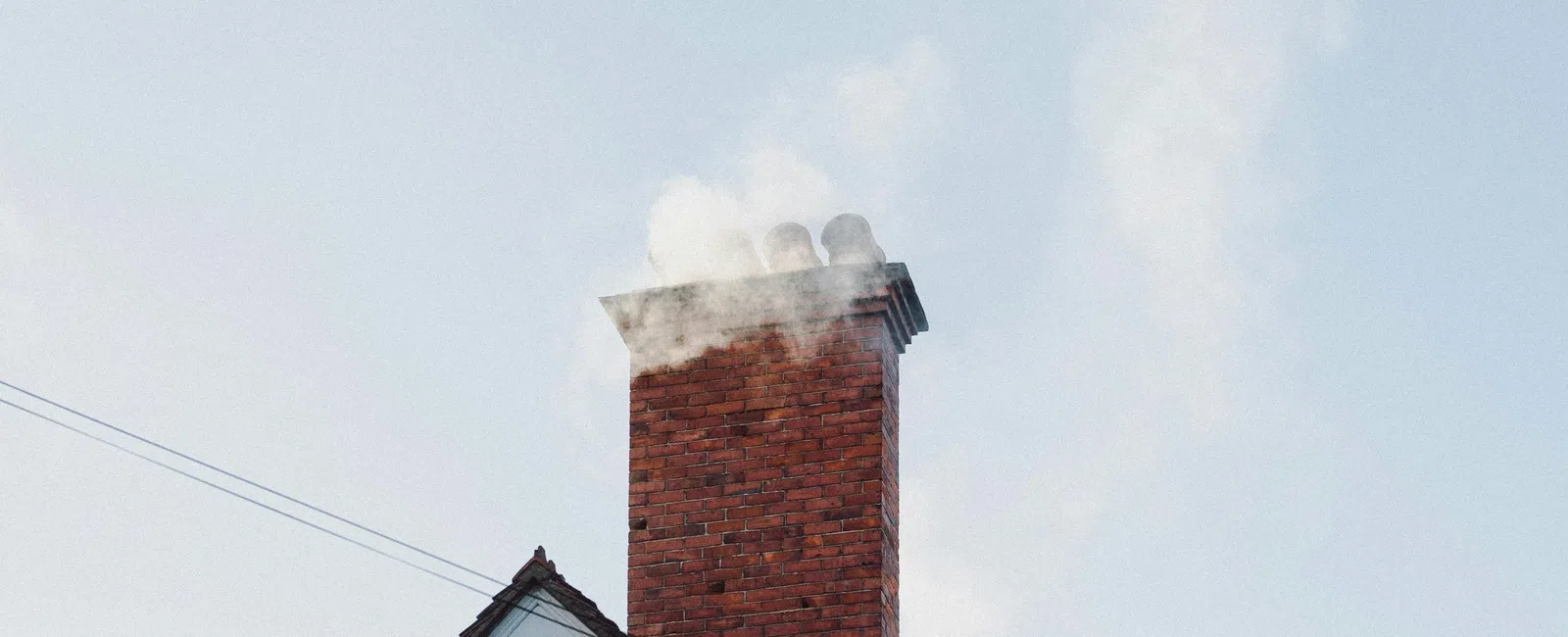 Brick chimney on a house with smoke rising against a clear blue sky during daytime.