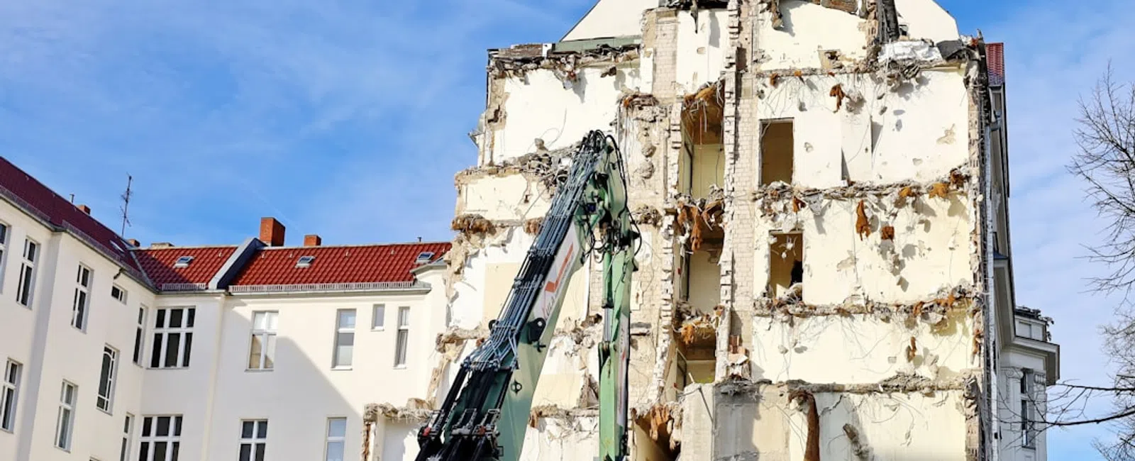 Partially demolished building facade with construction machinery against clear blue sky in urban area.