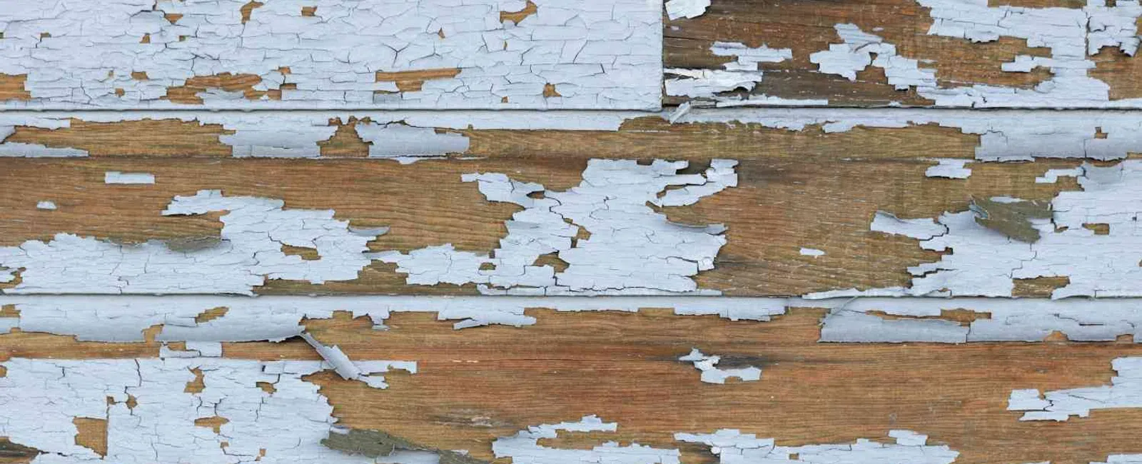 Close-up of wood panels with peeling light blue paint revealing natural brown wood beneath.
