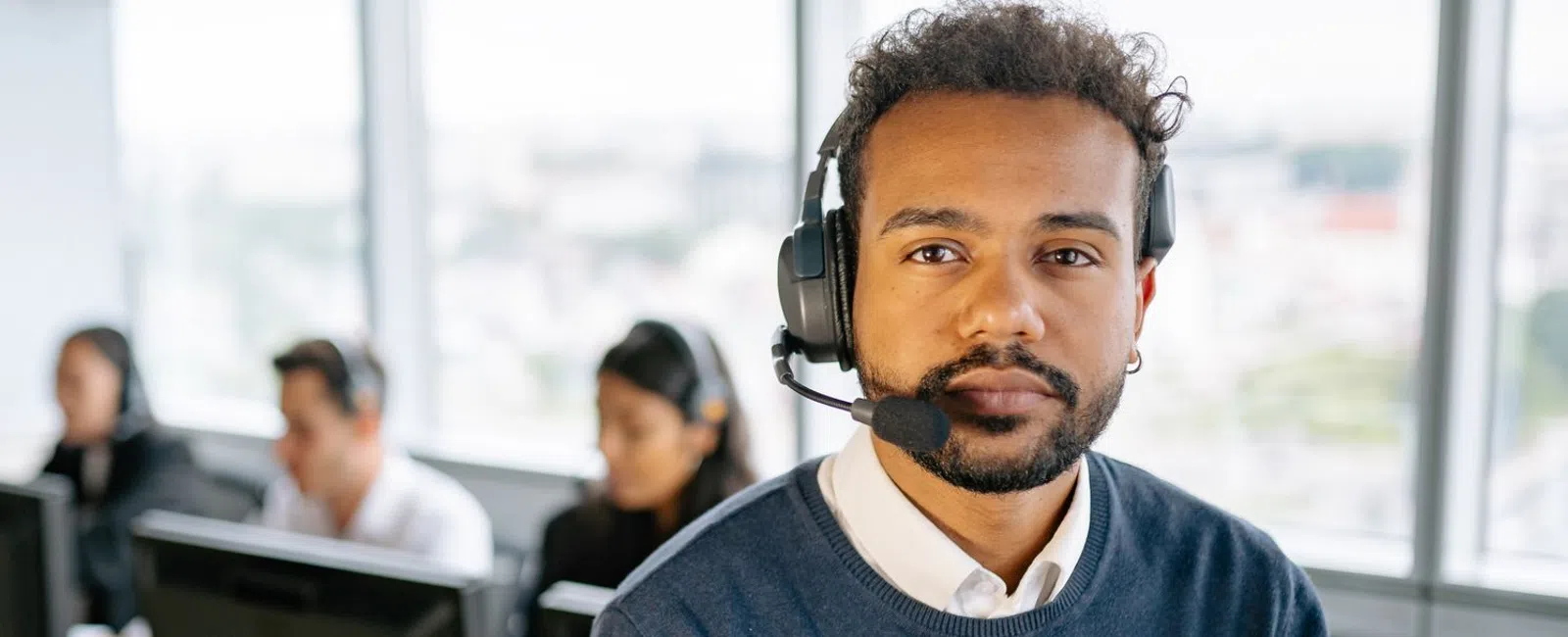 Customer service representative wearing headset in busy call center with colleagues working at computers