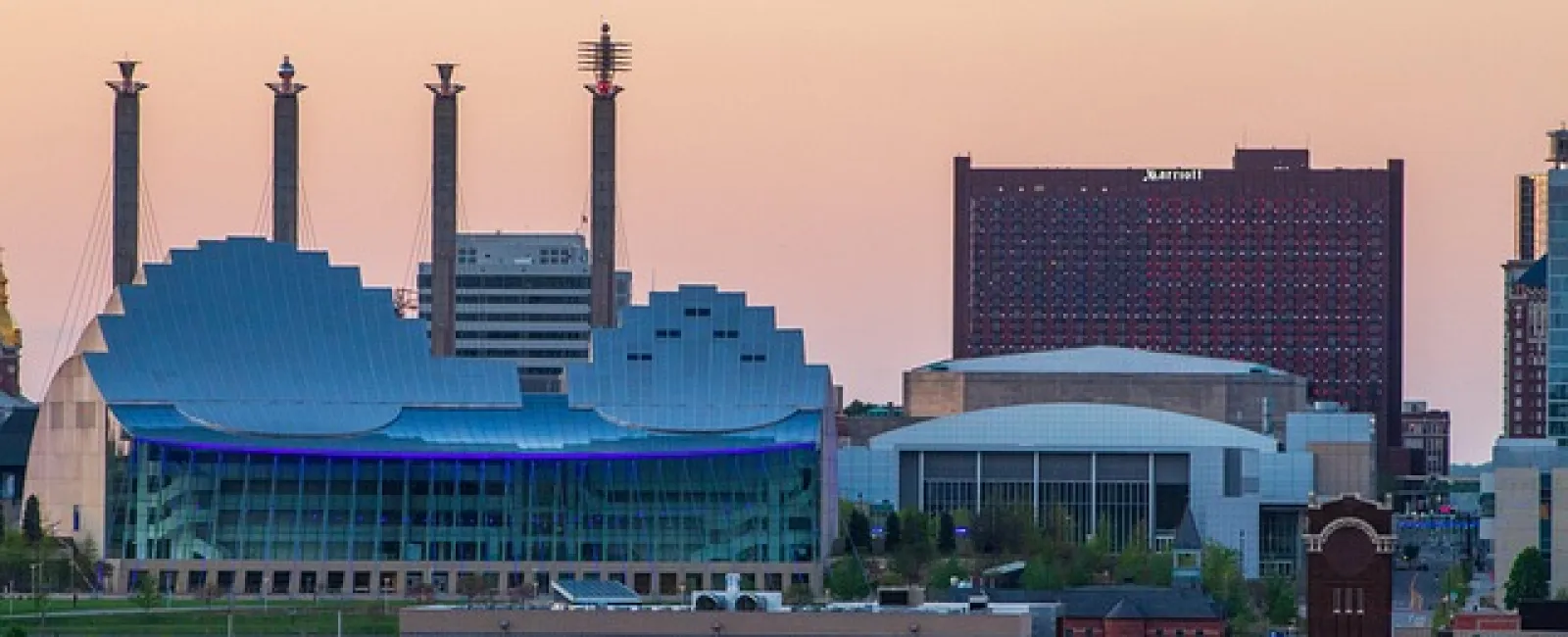 City skyline at dusk featuring the Kauffman Center with its distinctive curved roof and surrounding buildings.