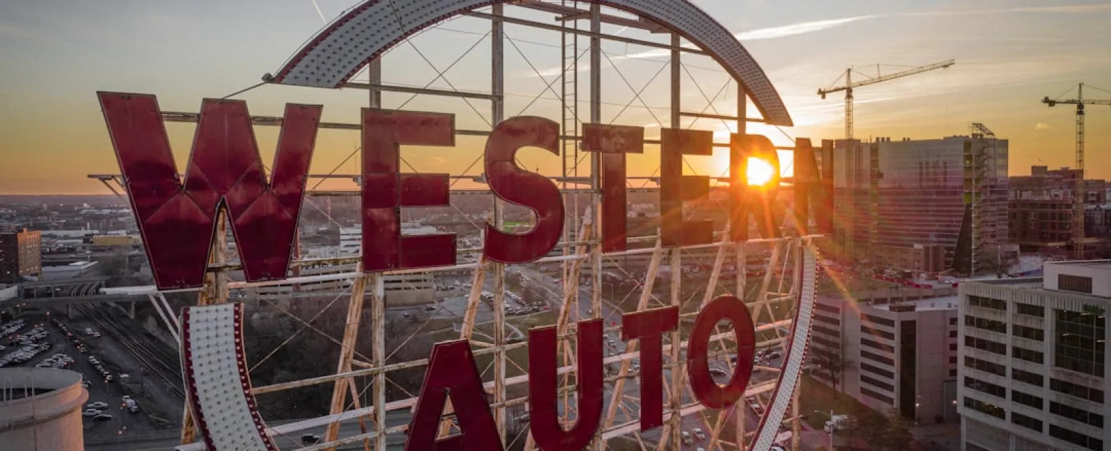 Vintage Western Auto sign at sunset with city skyline and construction cranes in the background.