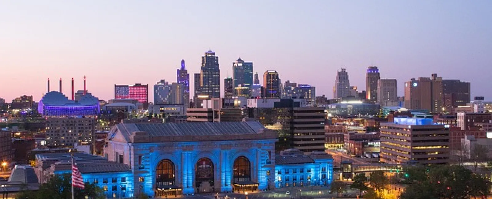 Twilight view of Kansas City skyline with Union Station illuminated in blue and city buildings glowing at dusk.