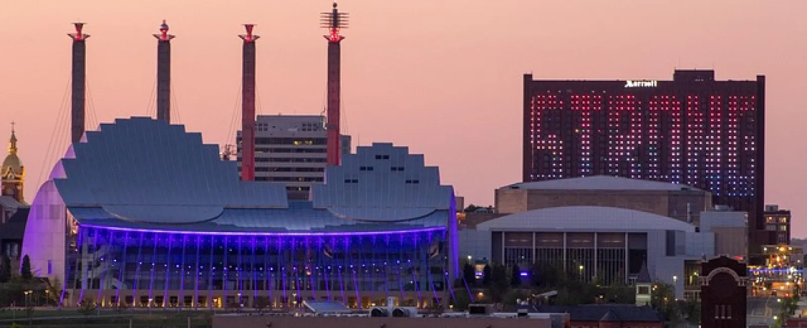 Downtown skyline at dusk with modern buildings and a hotel displaying a large illuminated STRONG sign.