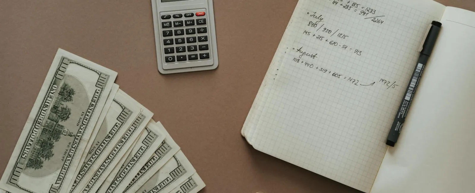 Flat lay of cash, calculator, notebook with handwritten notes, pen, and assorted coins on a brown surface