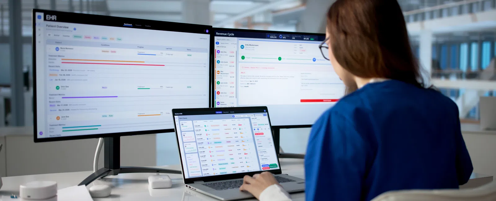 Healthcare professional using multiple screens to manage electronic health records and revenue cycle software.