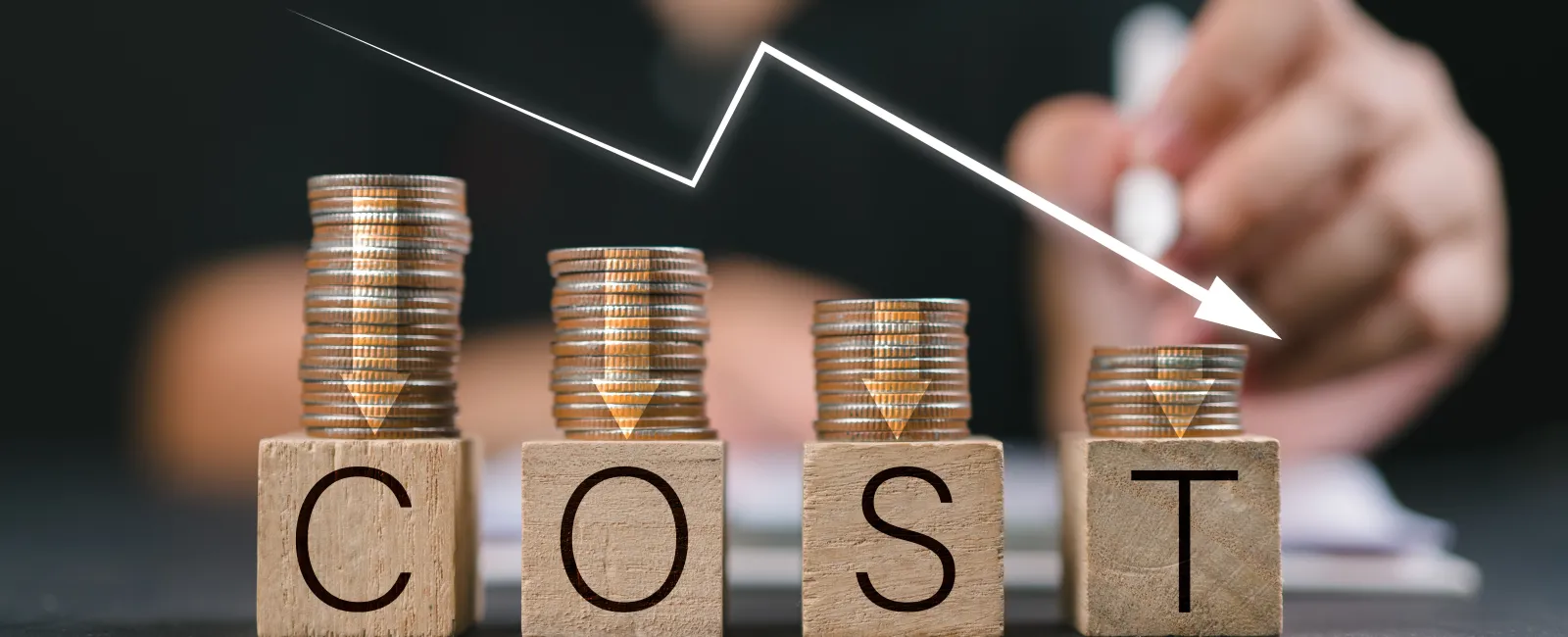 Wood blocks spelling COST with decreasing stacks of coins and a declining white arrow indicating reduced expenses.