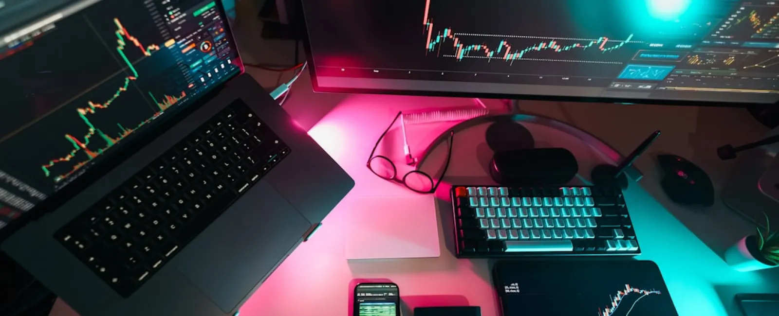 Multiple screens and devices displaying stock market charts and data with keyboard and calculator on desk.