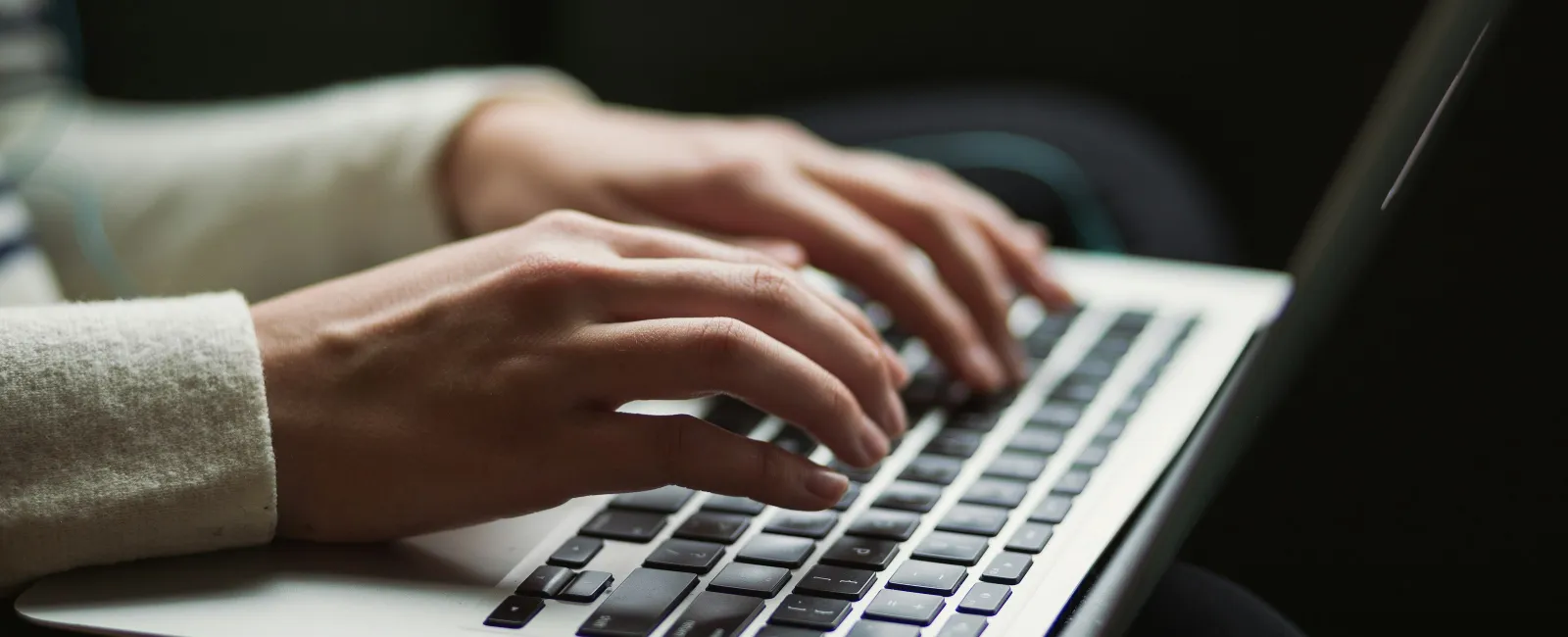 Close-up of person typing on a laptop keyboard with focus on hands and keys in low light