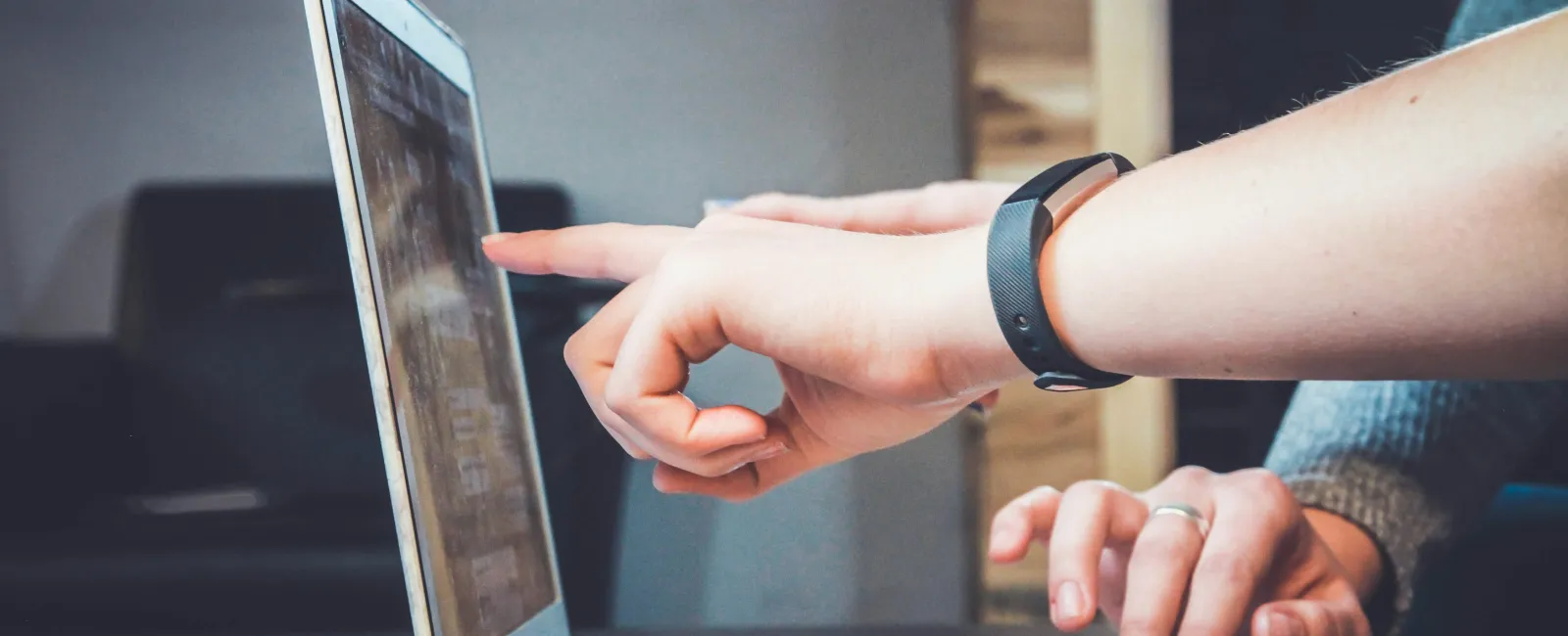 Person pointing at laptop screen while another types on keyboard in an indoor workspace setting
