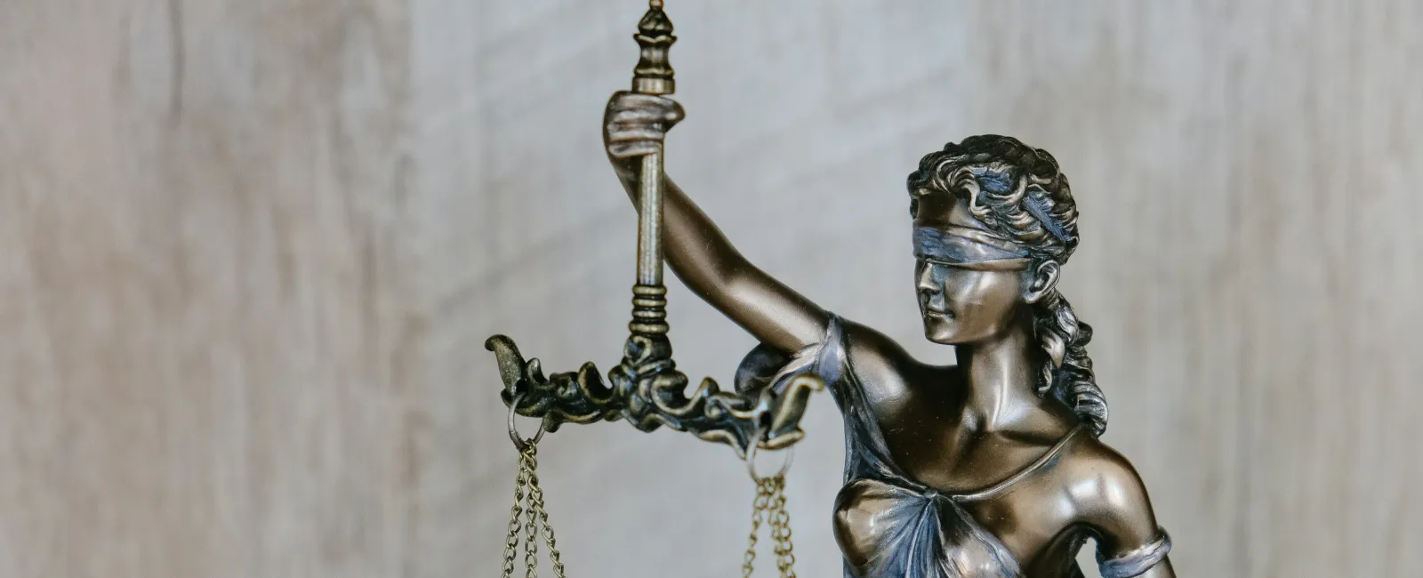 Bronze Lady Justice statue blindfolded holding balanced scales symbolizing fairness and law on wooden background