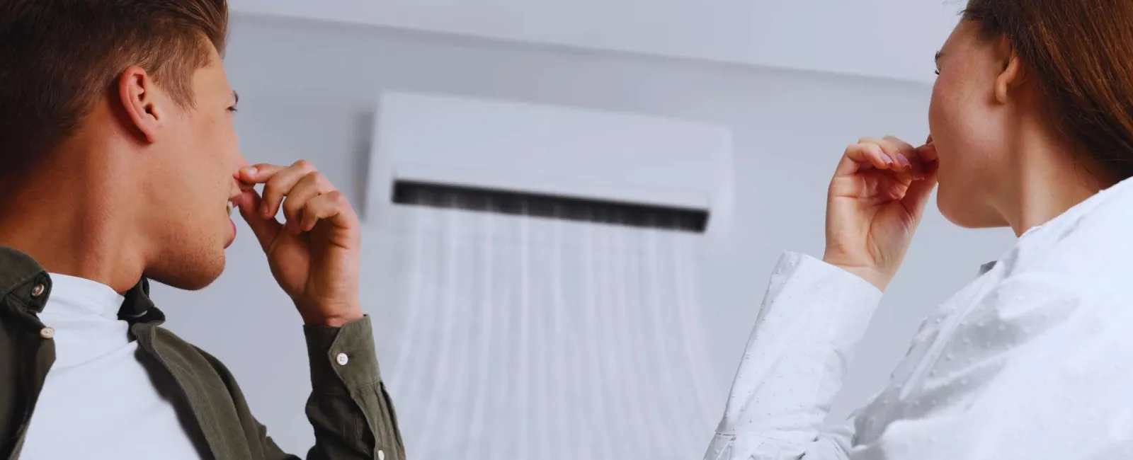Young man and woman holding noses reacting to bad smell from a running air conditioner indoors.