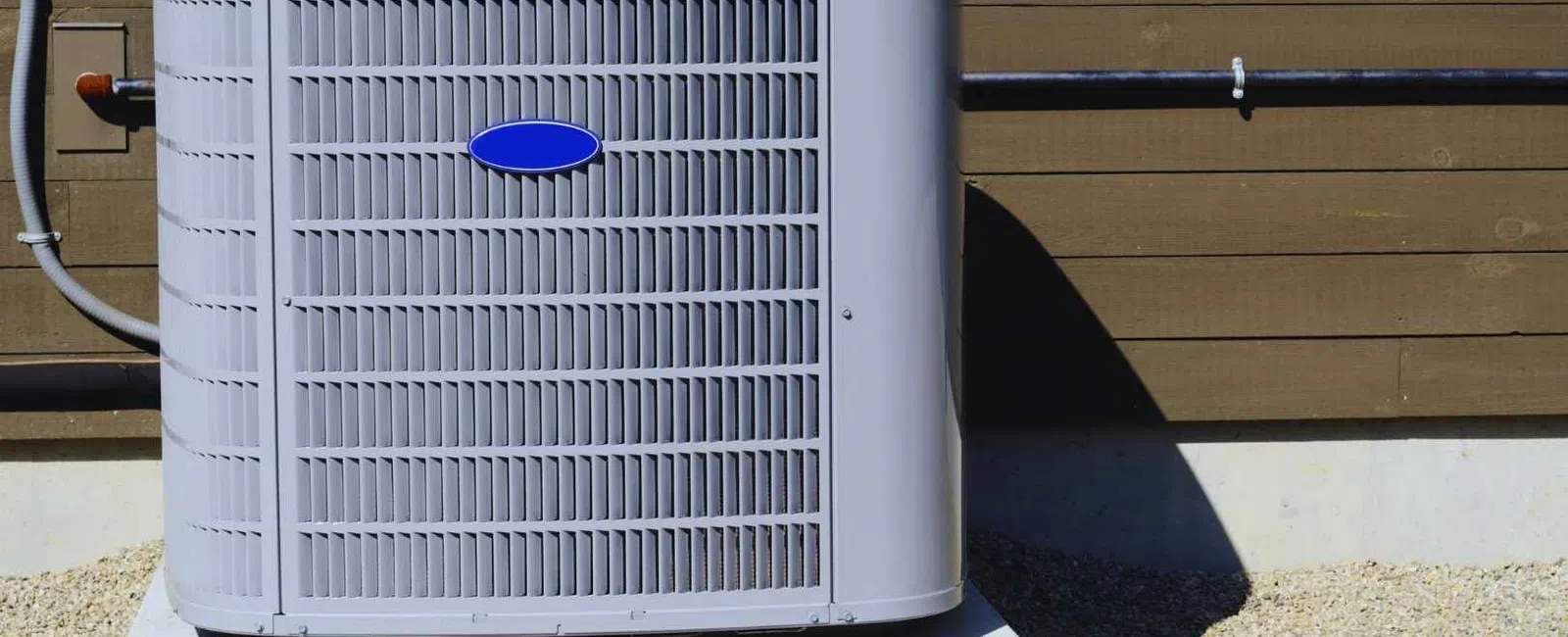 Outdoor central air conditioning unit installed on a concrete pad beside a wooden house exterior wall.