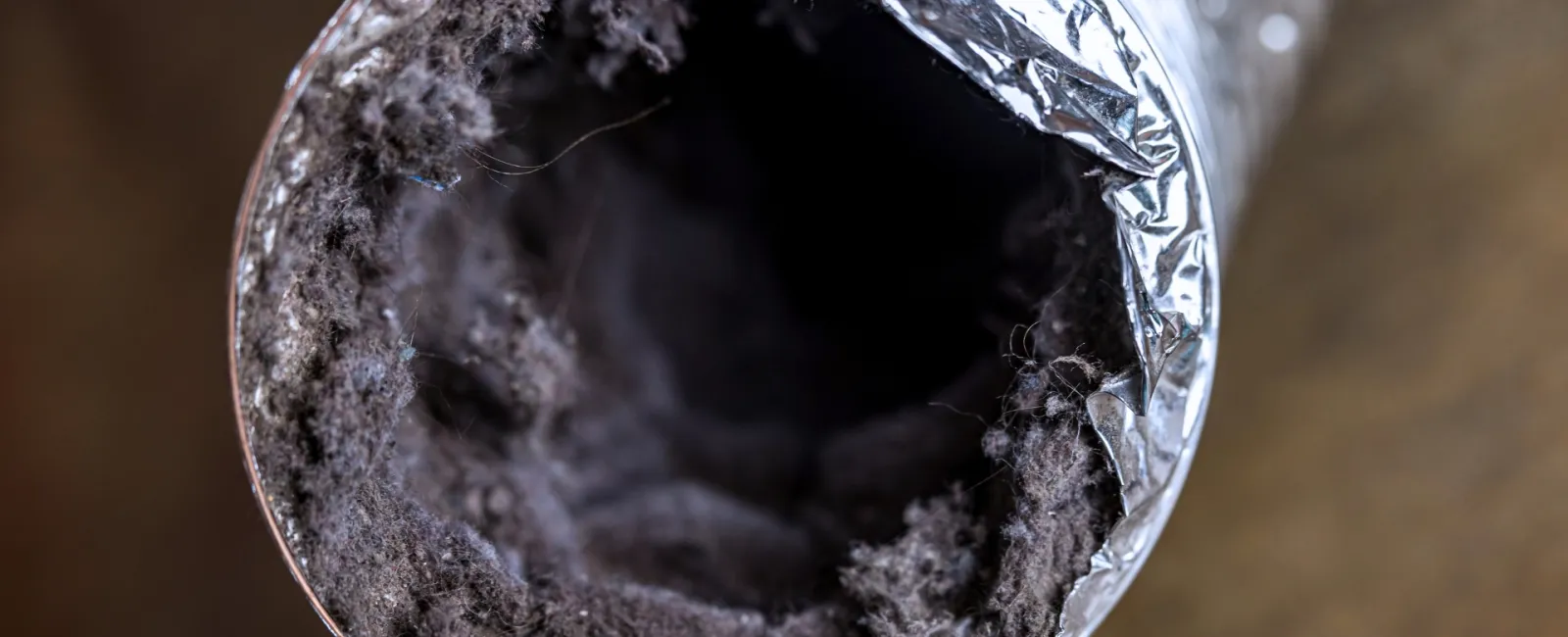Close-up of a heavily dust-clogged dryer vent duct with visible lint buildup inside.