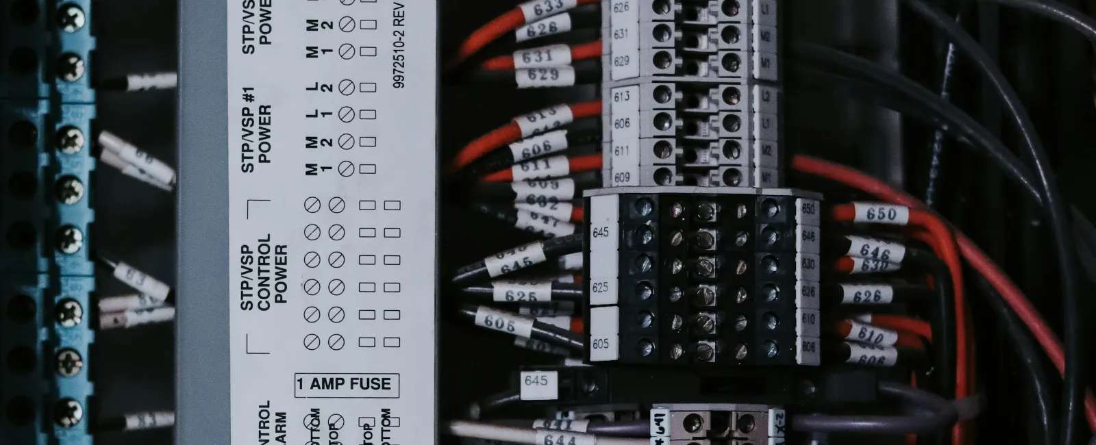 Close-up of an electrical panel with circuit breakers, labeled wires, and indicator lights glowing orange.