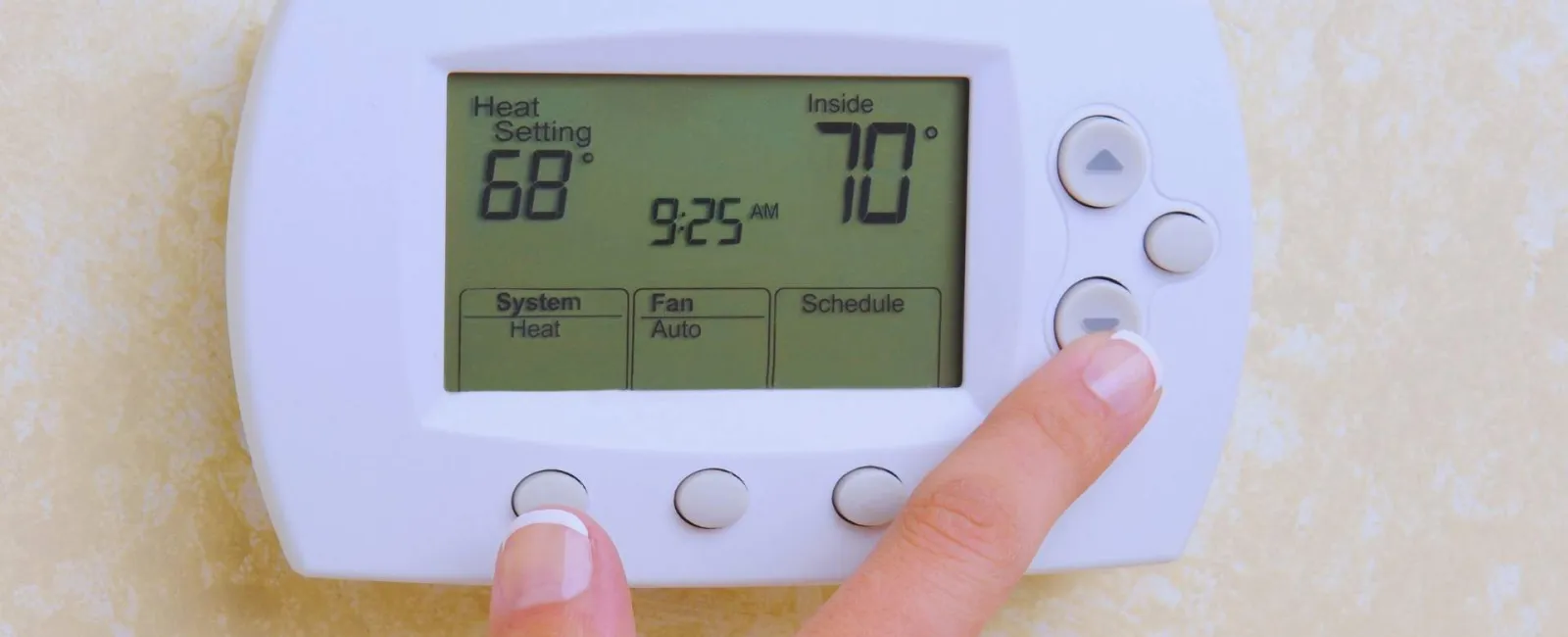 Close-up of hands adjusting a digital thermostat set to 68 degrees with indoor temperature of 70 degrees.
