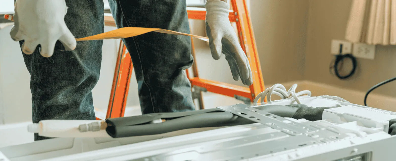 Technician measuring air conditioner unit with tape measure during installation in a room.