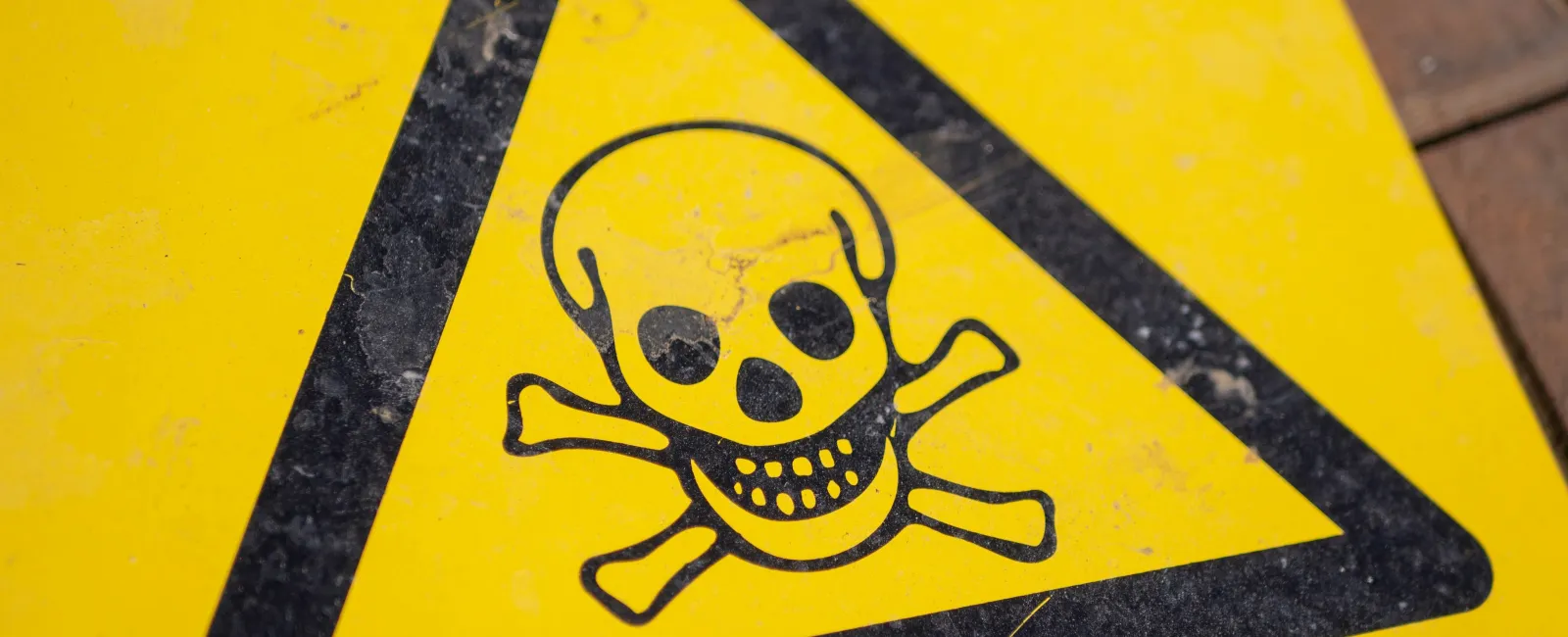 Close-up of a yellow warning sign with a black skull and crossbones indicating toxic or hazardous danger.