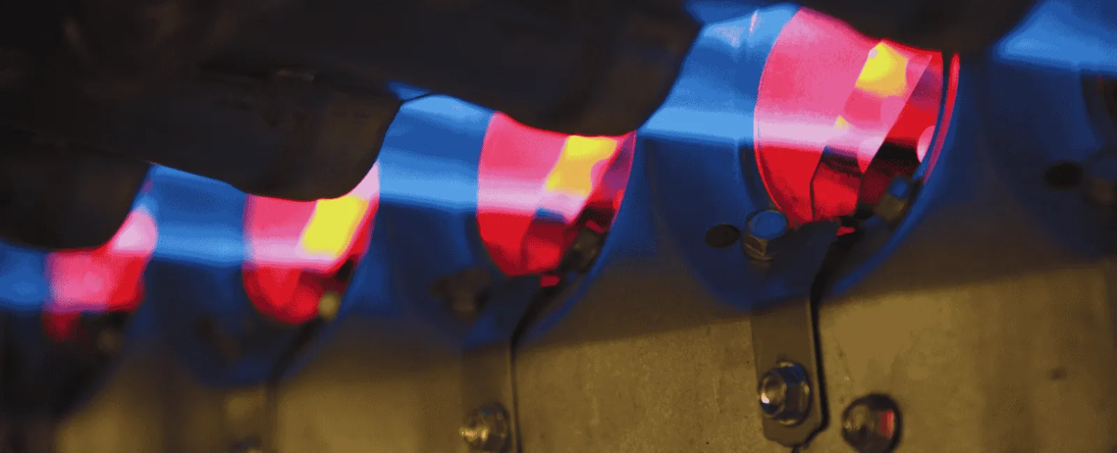 Close-up of blue and red gas flames burning in a row on a gas stove burner.