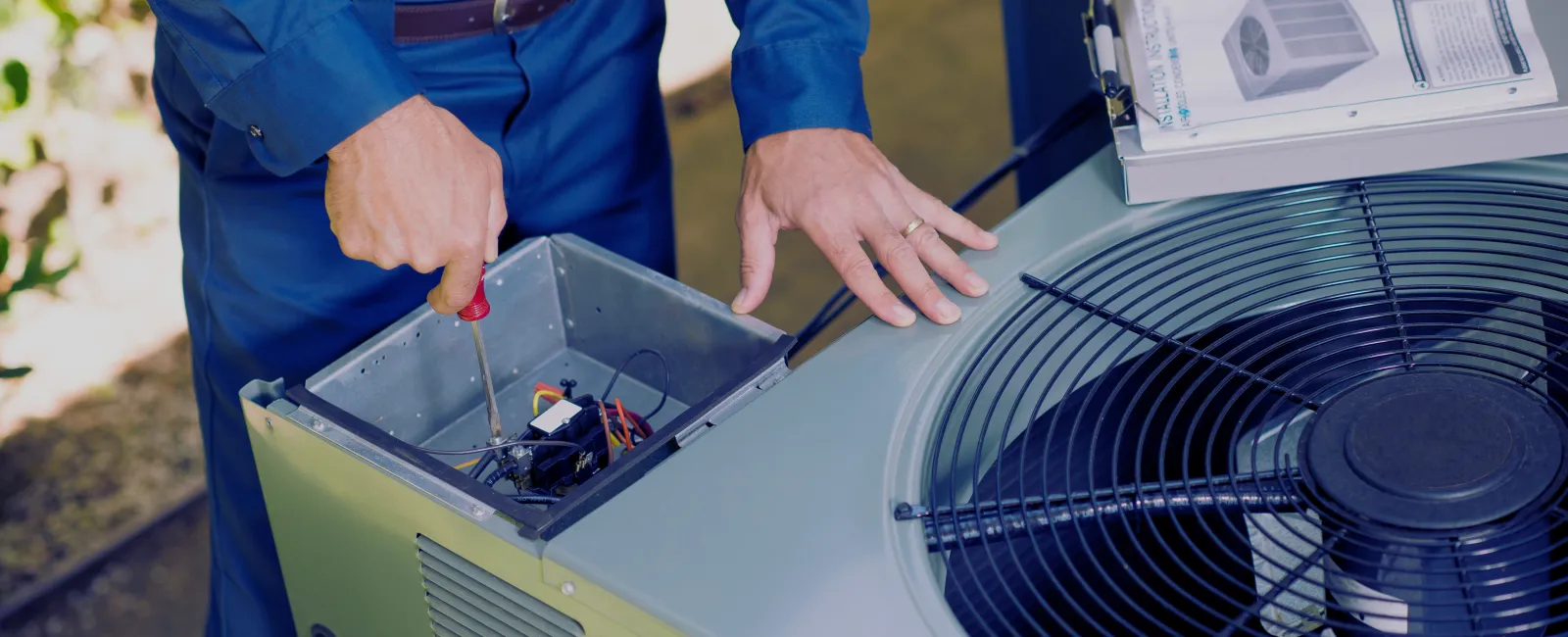 Technician repairing an outdoor air conditioning unit with screwdriver in a residential setting.