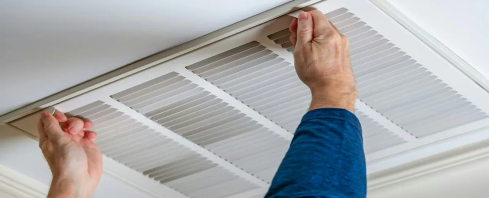 Person removing or installing a white ceiling air vent cover in a home interior.