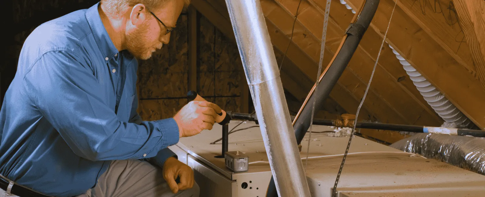 Technician inspecting and repairing HVAC system in an attic with tools and ductwork visible