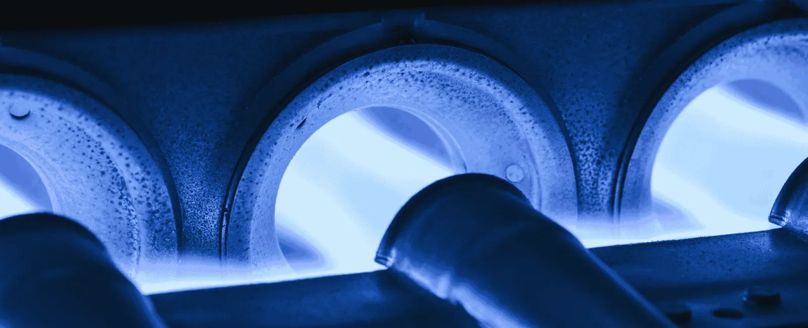 Close-up of blue gas flames burning inside a metal gas burner with pipes and vents glowing under heat.