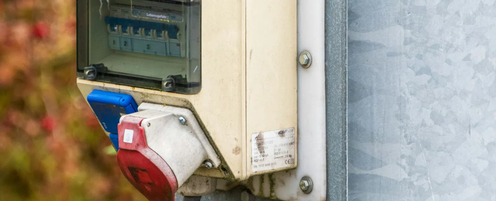 Outdoor electrical junction box with switches and industrial power plugs mounted on a metal pole.