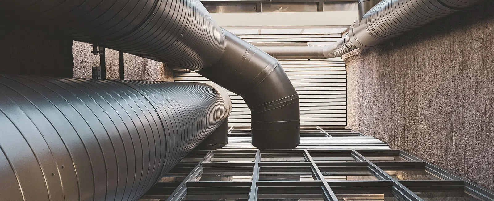 Industrial metal ventilation ducts above modern building windows and walls under a skylight ceiling.