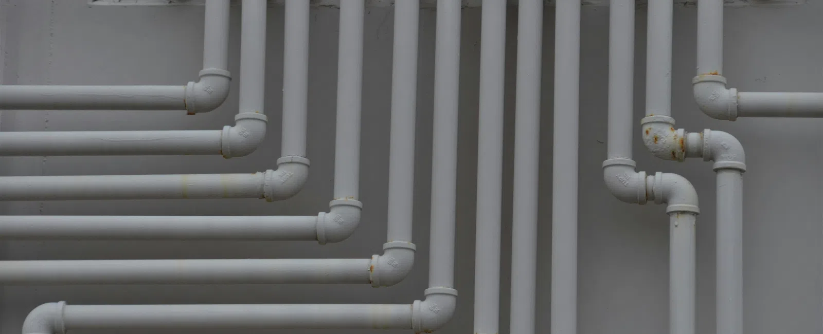 White PVC pipes arranged vertically and horizontally on a gray wall forming a complex plumbing network.